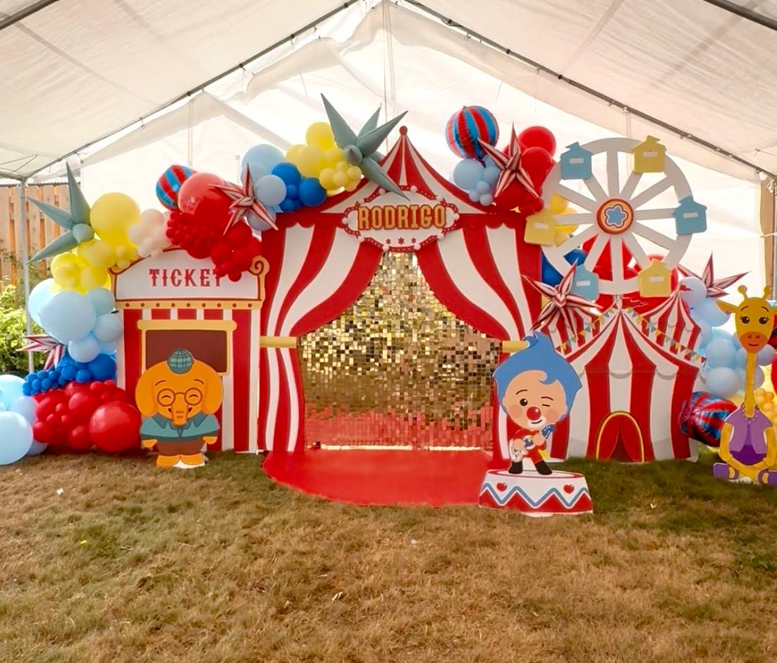 Colorful circus birthday backdrop with balloons, carnival props, and gold sequin wall