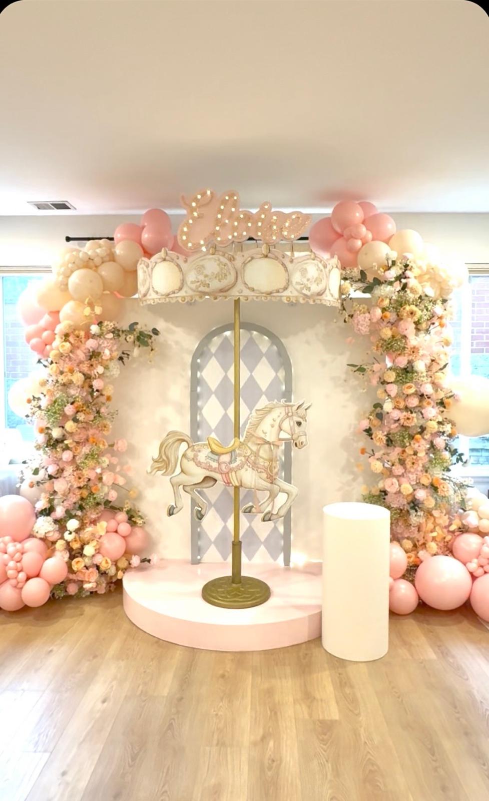 Pastel carousel-themed celebration backdrop with florals and balloons
